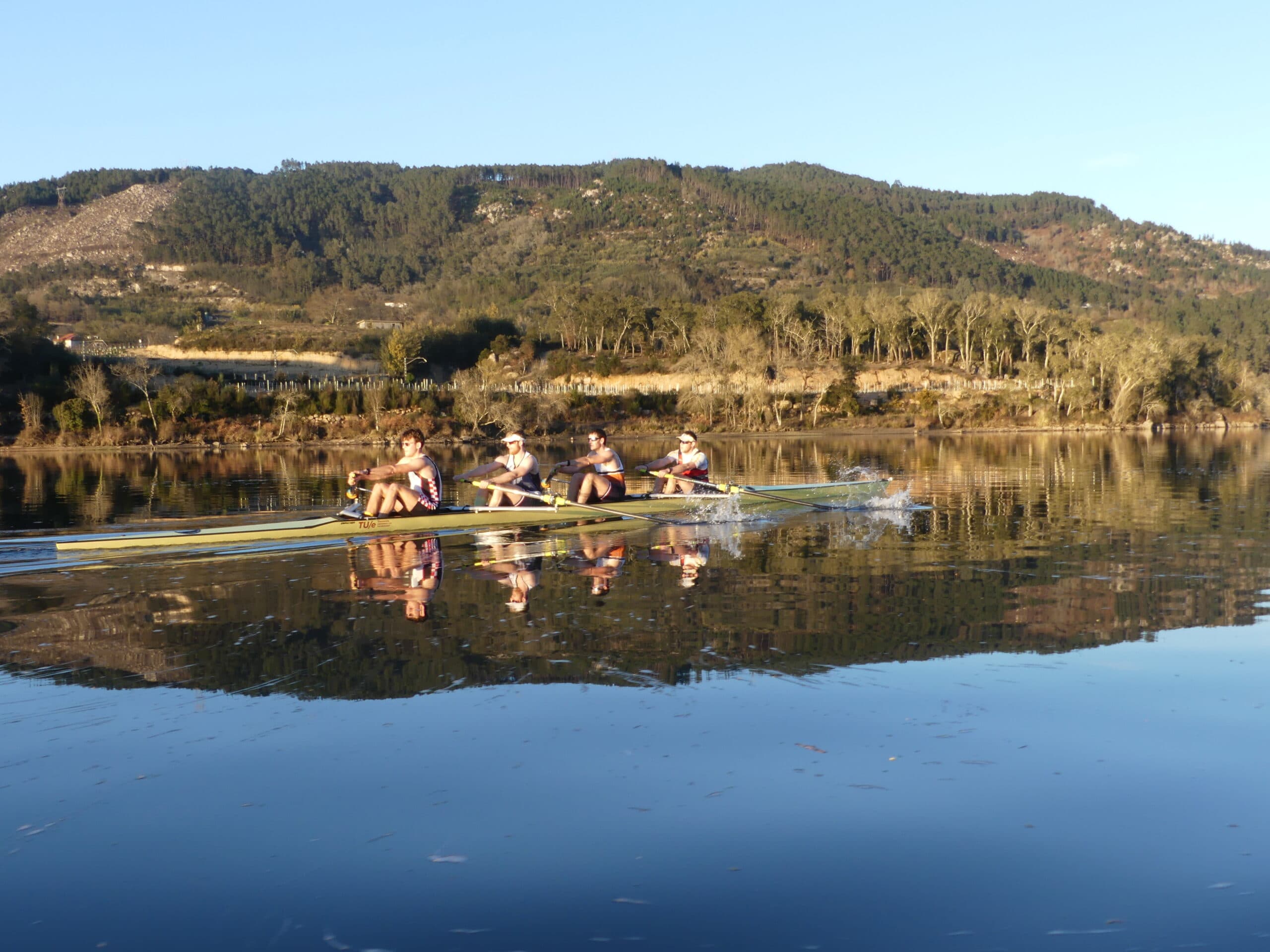 Four rowers moving across a calm river